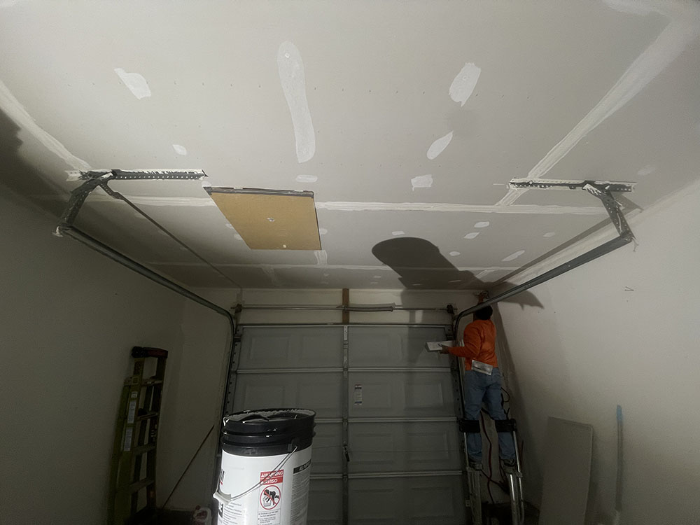 Finisher embedding tape along ceiling seams near overhead roll-up garage door